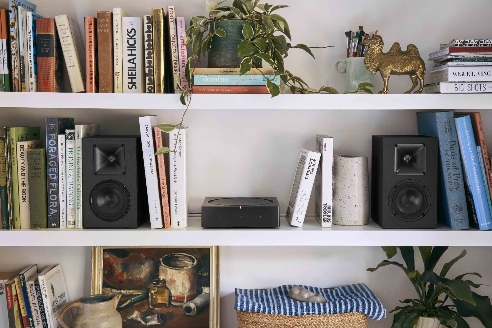 Sonos speakers and a streaming amp styled on a white bookshelf with books and decor.