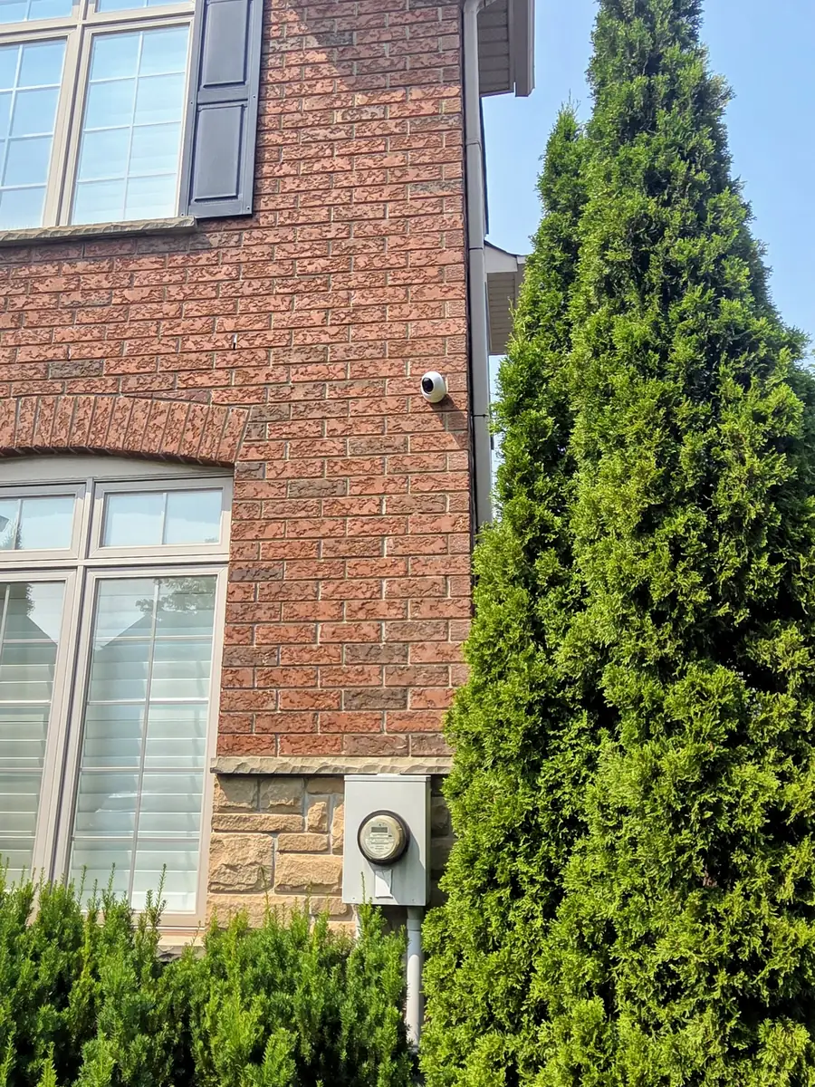 Finished exterior of an Oakville brick home showing a discreet UniFi camera with no visible cable running along the brick, soffit, or fascia