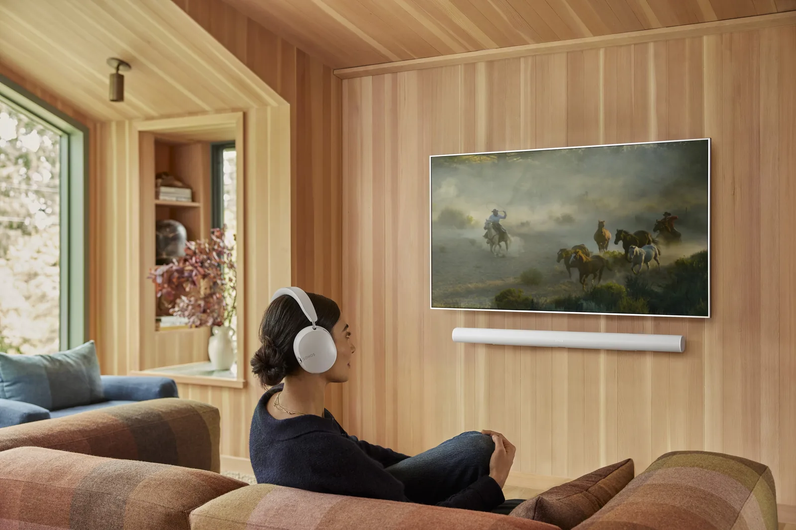 Woman wearing Sonos Ace headphones watching TV, with a Sonos Arc Ultra soundbar below the screen