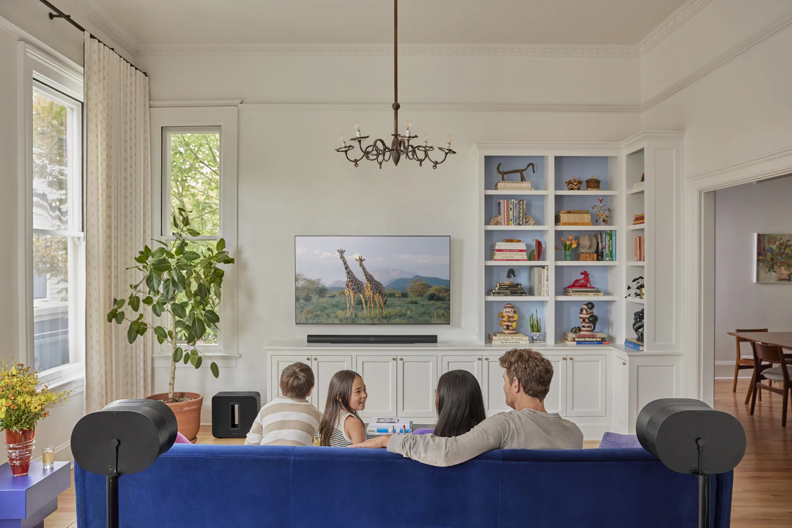 Family watching TV with a Sonos soundbar, subwoofer and two rear surround speakers