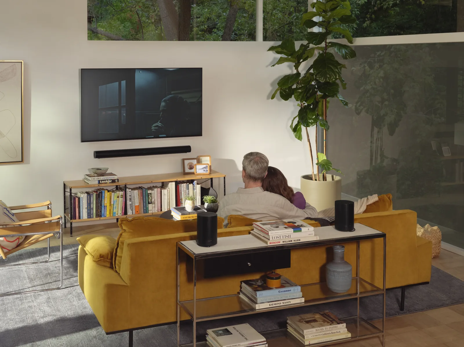 Couple watching TV with a Sonos soundbar and speakers in a living room