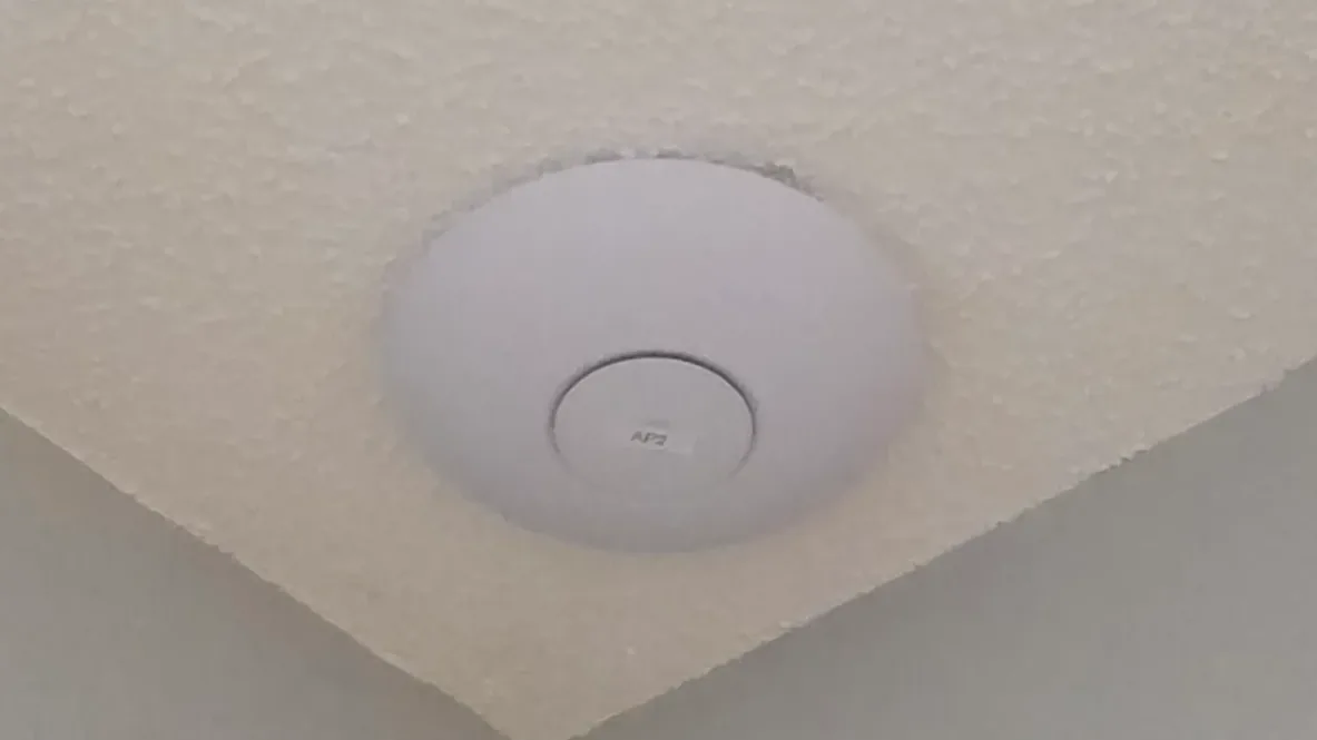 UniFi ceiling access point mounted near a corner in a finished home