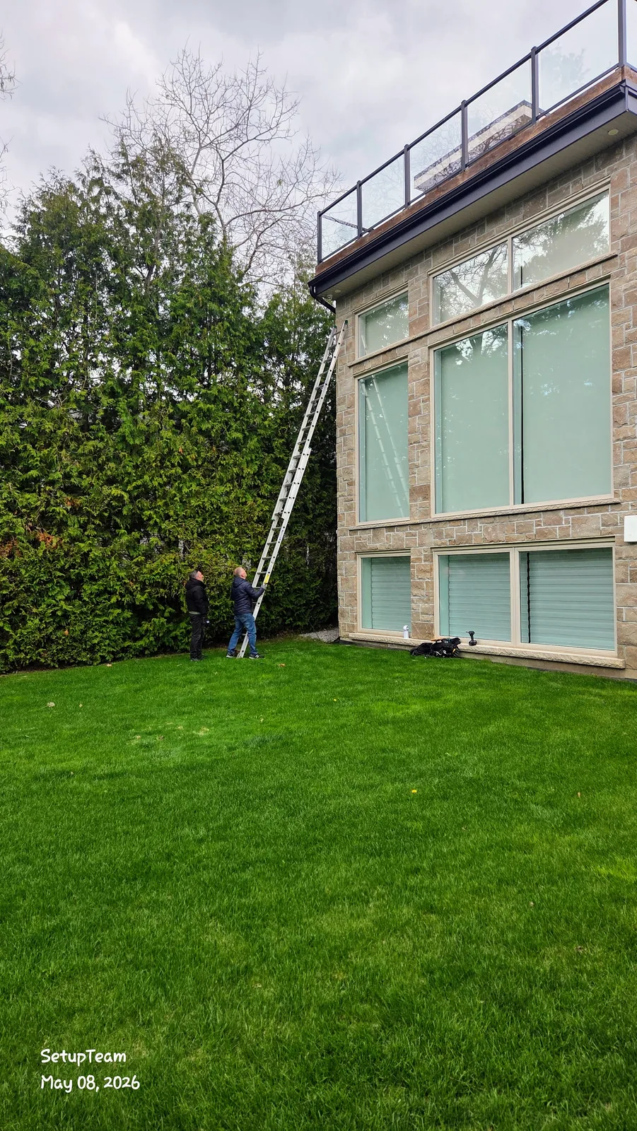 Two SetupTeam installers positioning an extension ladder against a stone home to mount an exterior security camera