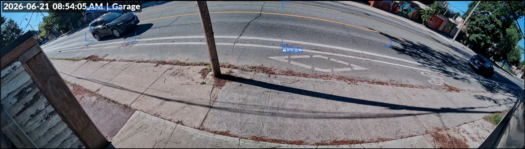 UniFi G6 180 camera view from the back of a garage showing a full 180-degree sweep of the driveway, sidewalk and street — wide-area coverage with minimal blind spots