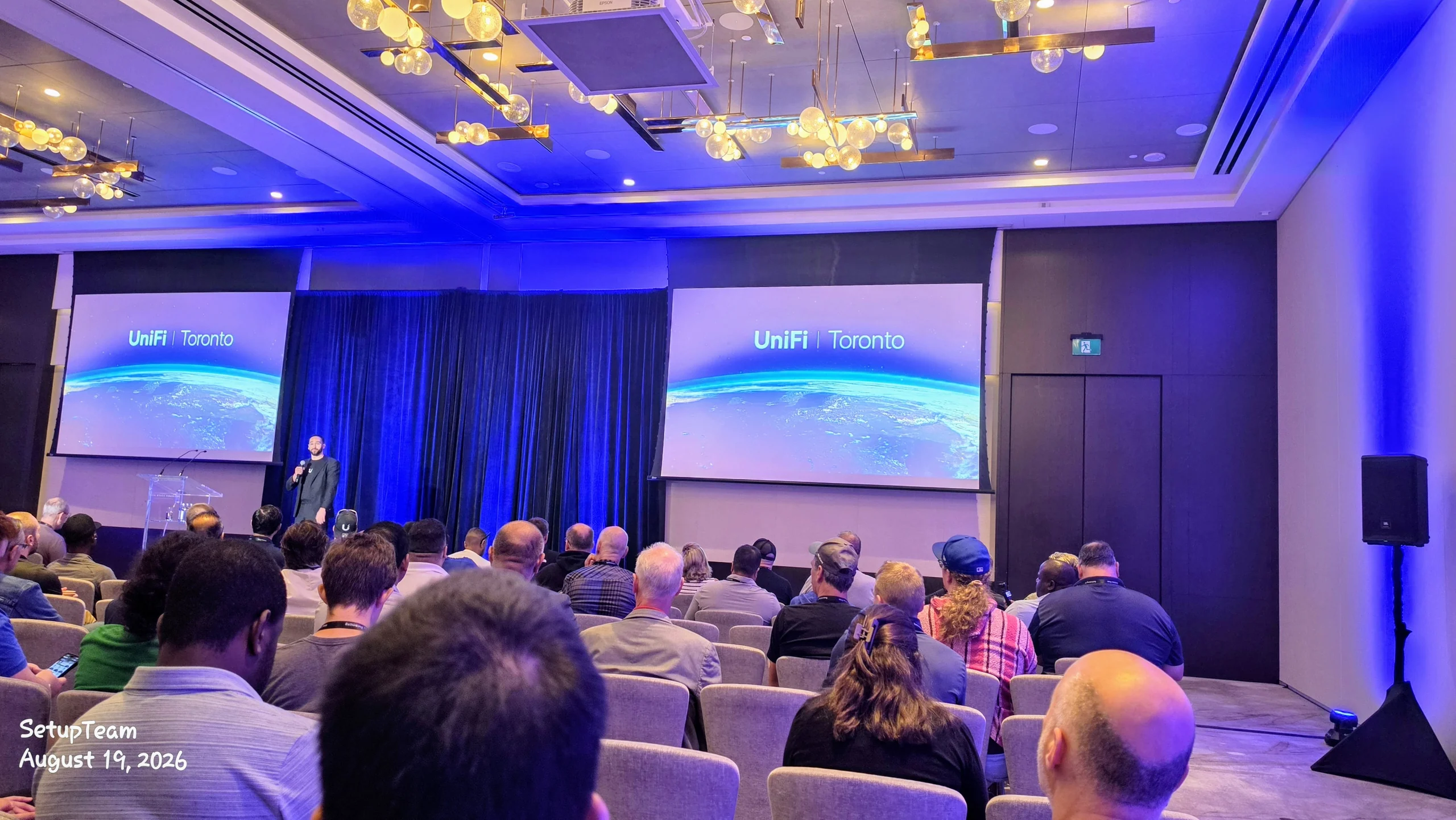 A full ballroom audience at the UniFi Toronto Conference keynote, with twin screens reading UniFi Toronto