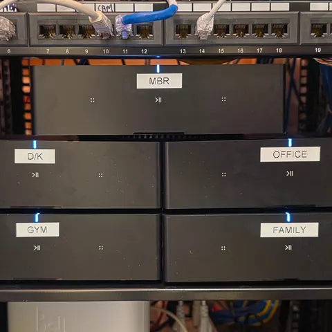 Control4 audio distribution upgraded with five dedicated Sonos Amps in a network rack, each labelled by room, powering a home theatre and whole-home audio, completed by SetupTeam.
