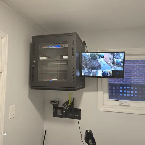 Wall-mounted network rack installation with security camera monitoring display and structured networking equipment in Newmarket.