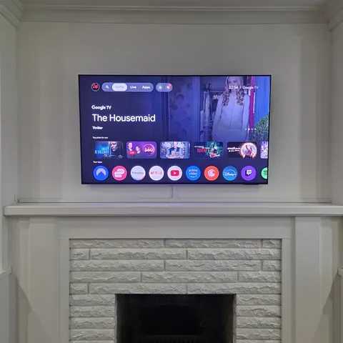 TV wall mounting installation above a painted white brick fireplace with concealed wiring and centered placement in Newmarket.