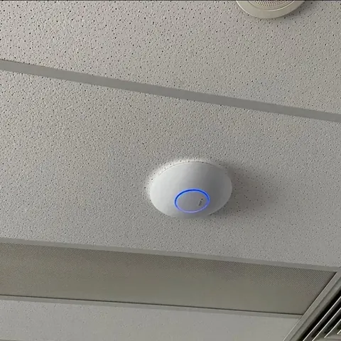 UniFi ceiling-mounted Wi-Fi access point installed in a suspended tile ceiling, status LED ring lit