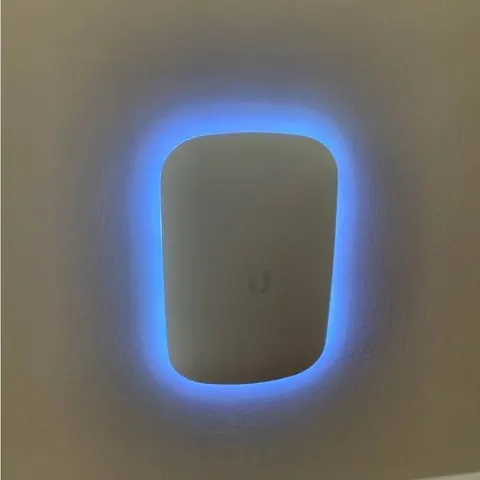 UniFi Wi-Fi extender wall-mounted on a painted interior wall, status LED ring lit
