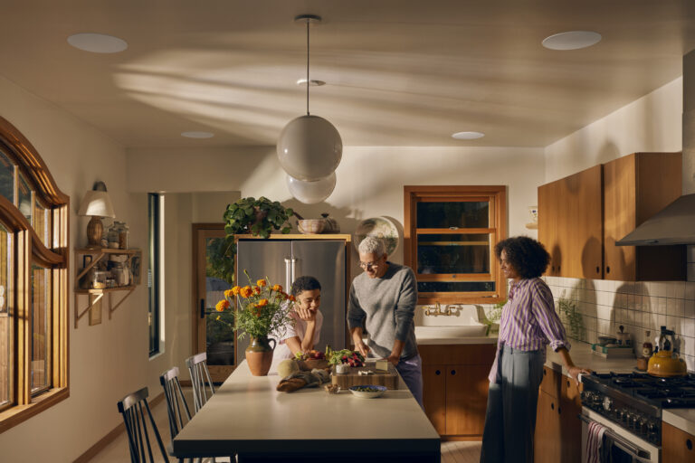 People gathered around a kitchen island in a modern home with warm natural light.