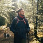 Outdoor portrait of a man with a backpack standing in a sunlit forest.