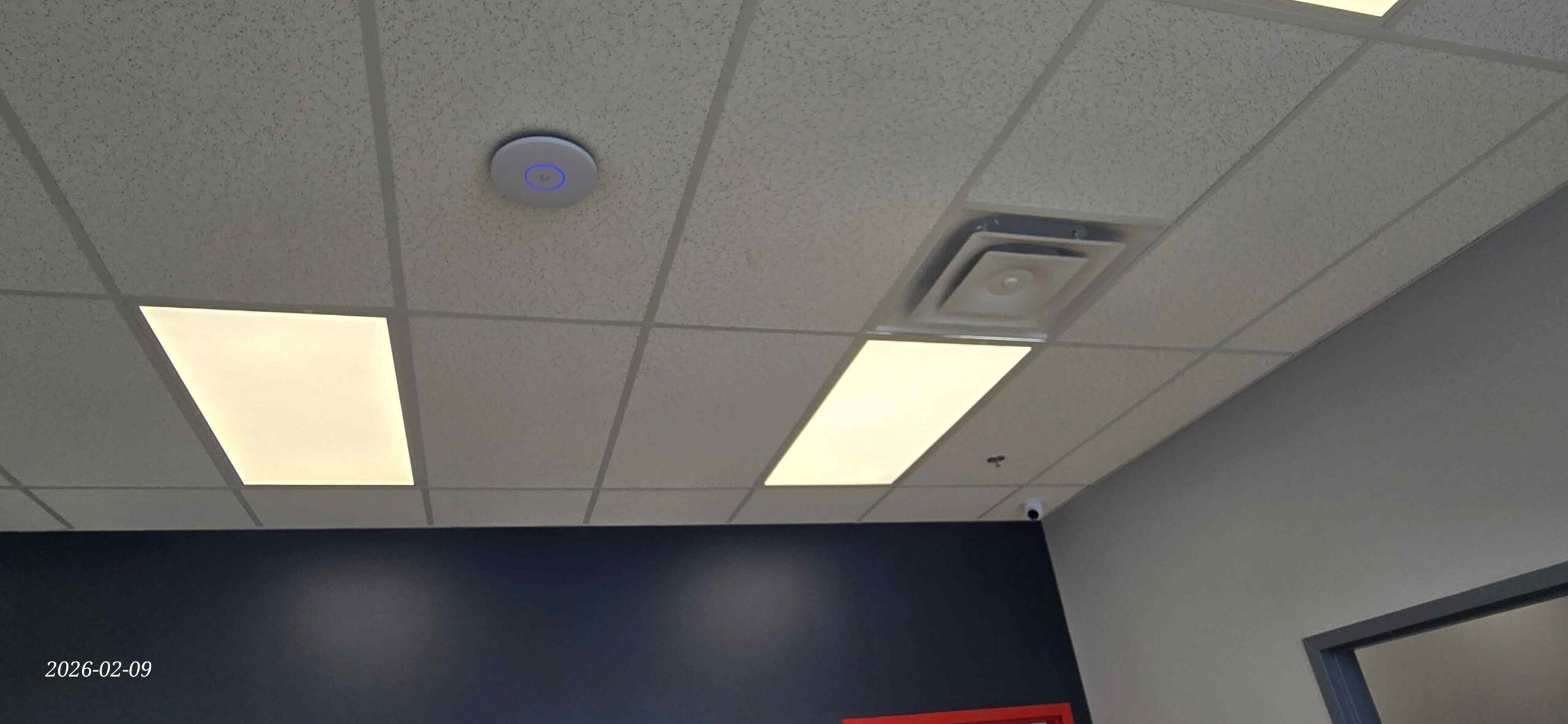 UniFi access point mounted on a suspended ceiling in a commercial interior