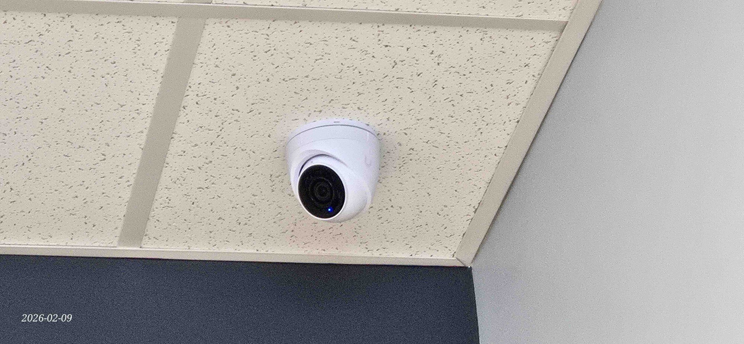 UniFi Protect security camera mounted on a ceiling tile in a commercial interior
