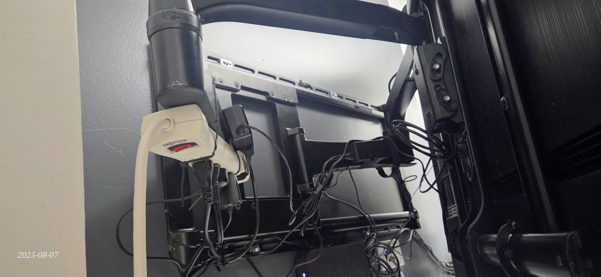 Messy cables behind full-motion TV wall mount arm showing why in-wall cable management is the better solution