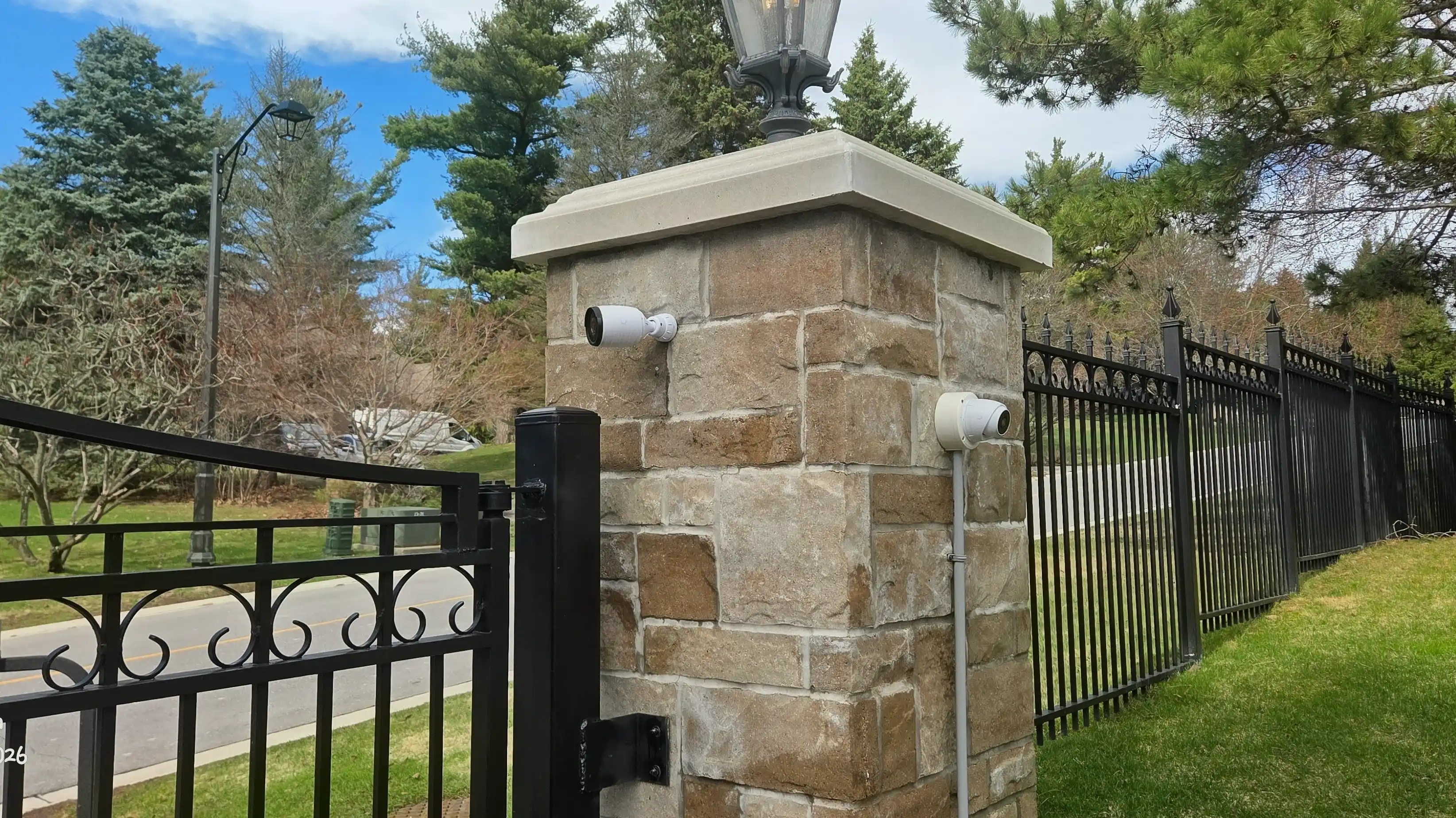 UniFi Protect security cameras installed on a stone gate pillar at a gated residential driveway