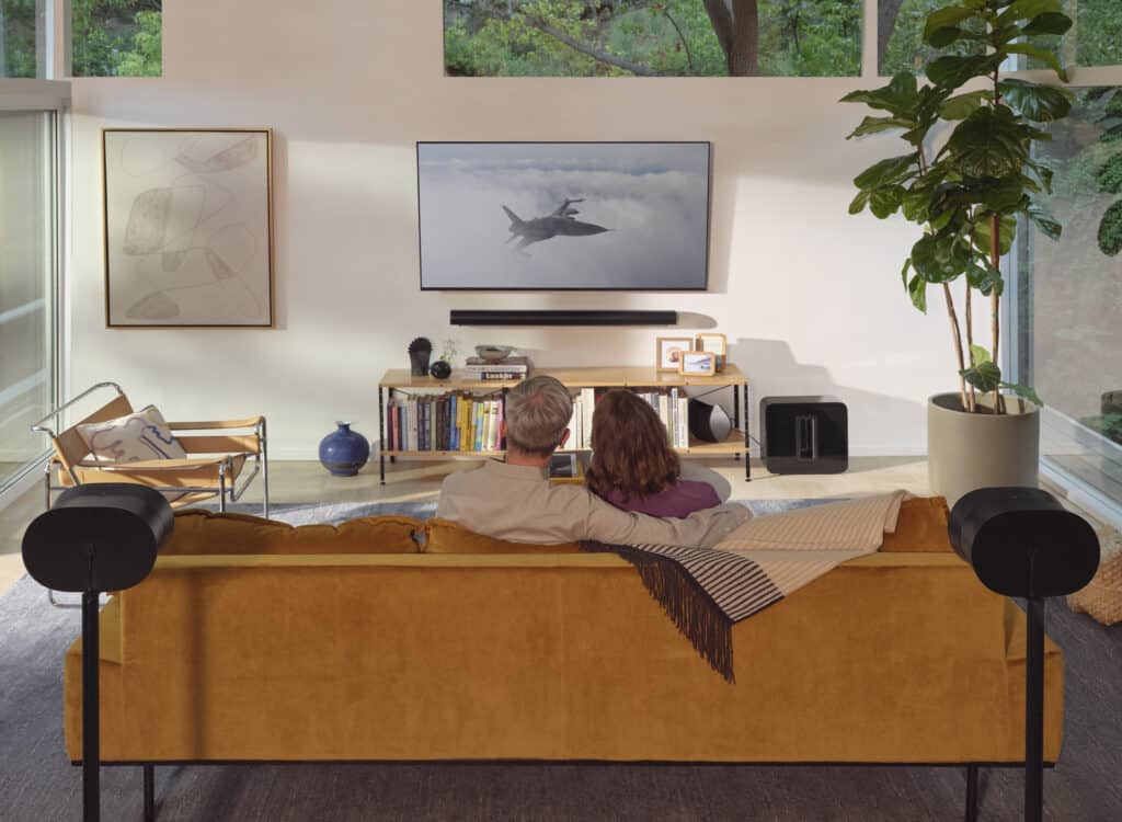 A couple enjoying a professionally installed Sonos home theater system, featuring a soundbar, wireless subwoofer, and discreet rear surround sound speakers, integrated into a modern smart home living room for optimal audio-visual entertainment